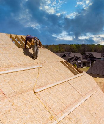 Workers applying nailing plywood panels a roof on the new house