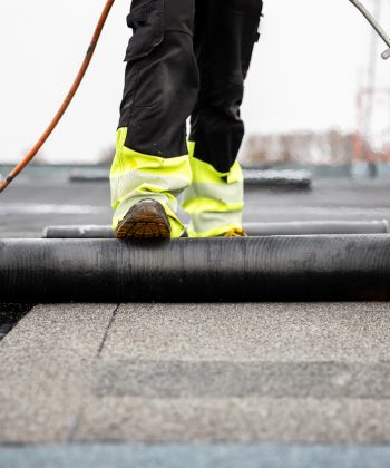 professional roofer applying tar with blowtorch on new roofing felt for waterproofing a flat roof construction site with safety gear
